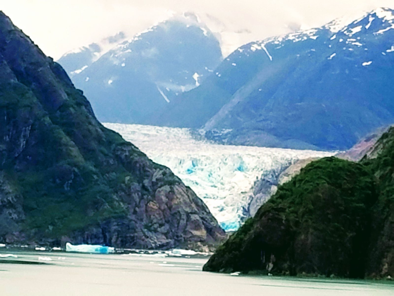 Sawyer Glacier at the head of Tracy Arm, a broad blue and white glacier face between dark mountain walls, with ice on the water