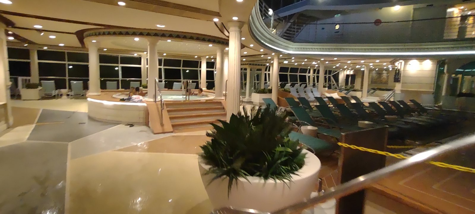 An empty pool deck on a cruise ship at night, loungers stacked and the whirlpools lit