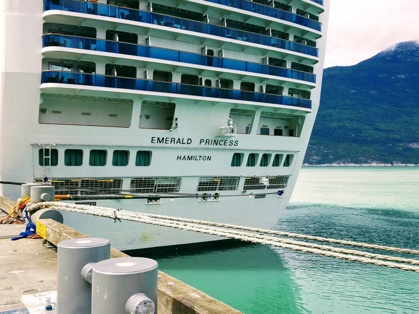 The stern of the cruise ship Emerald Princess tied up at Skagway, with EMERALD PRINCESS and HAMILTON painted on the transom and green water below
