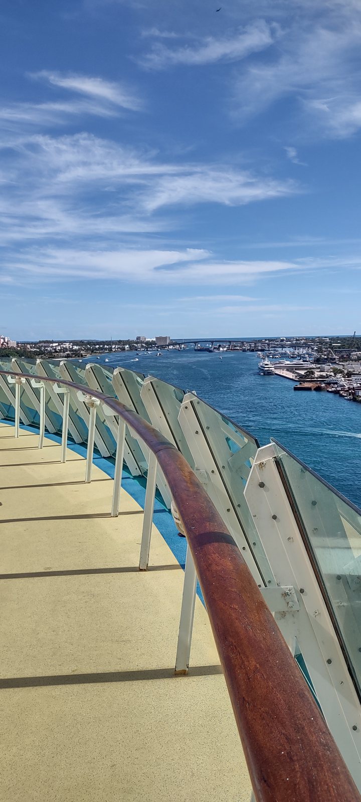 A cruise ship's lifeboats hanging along the side of the deck, with a port in the distance