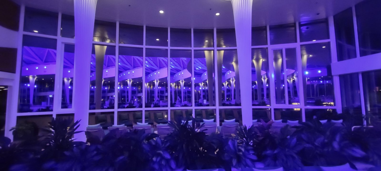 A ship lounge lit deep purple at night, tall windows looking out into the dark